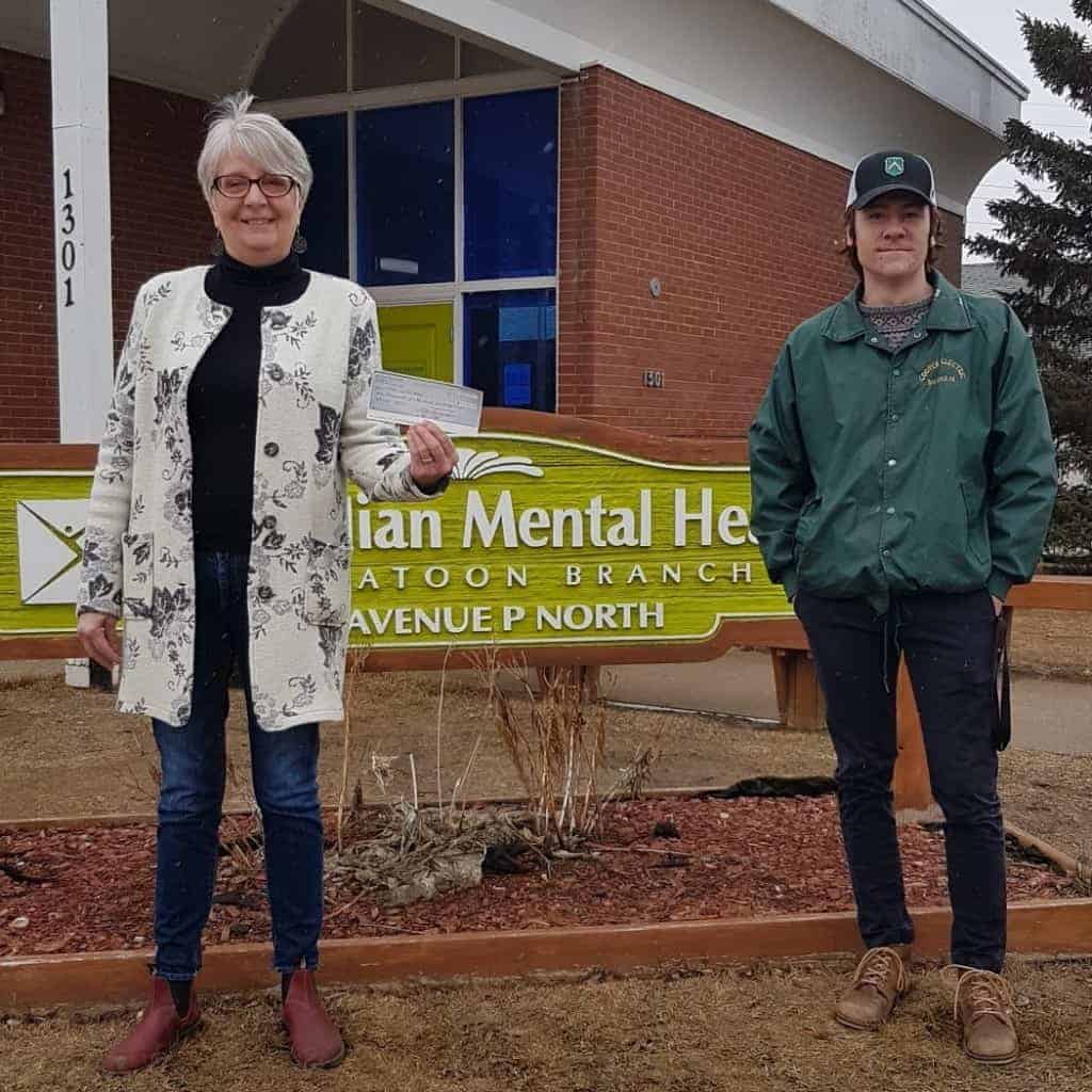 Faith and Kale are standing in front of the CMHA Saskatoon sign, holding a cheque that Kale donated.